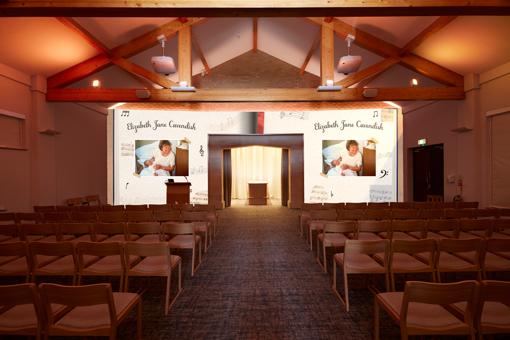 Audience seating in a small auditorium with a stage and two large screens displaying a tribute to Elizabeth Jane Cavendish, featuring a photo of her with a child and musical notes in the background.