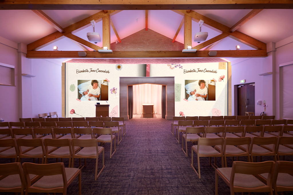 An indoor event space with rows of wooden chairs facing a stage with a large screen. The screen displays a photo of a woman and a child, with text "Elizabeth Jane Cavendish" and decorative flowers around it.
