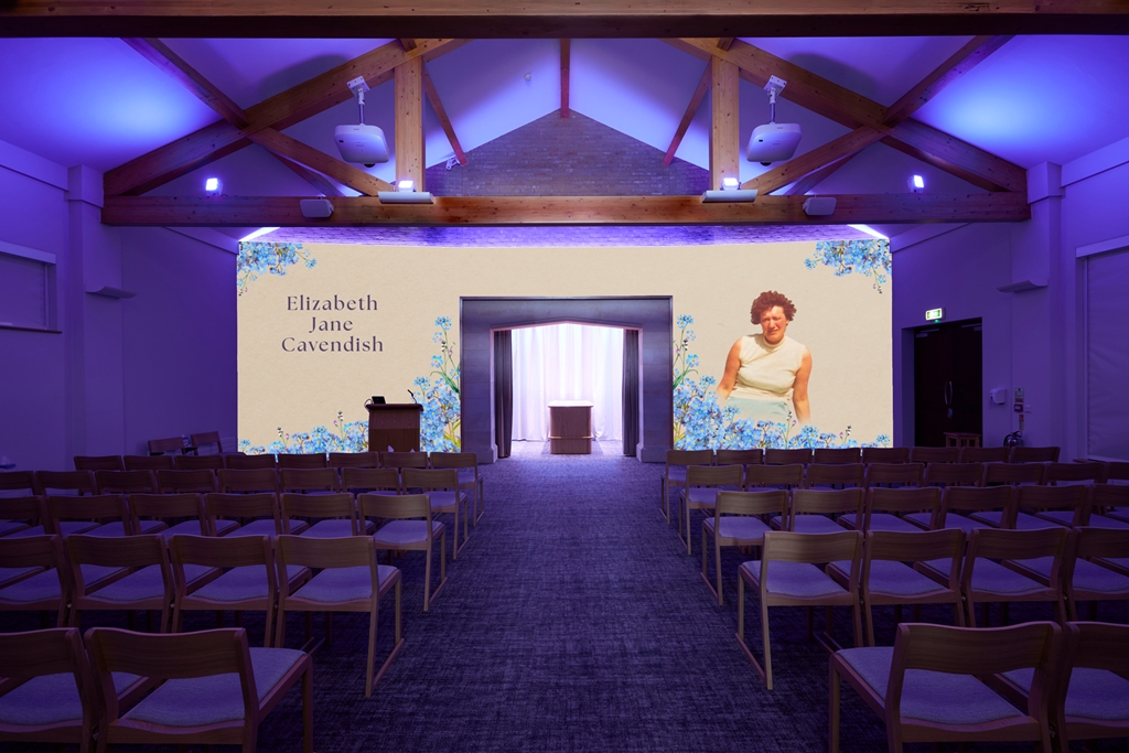 Conference room with rows of chairs facing a large screen displaying the name Elizabeth Jane Cavendish and a picture of a woman in a white top, with wooden beams and purple lighting