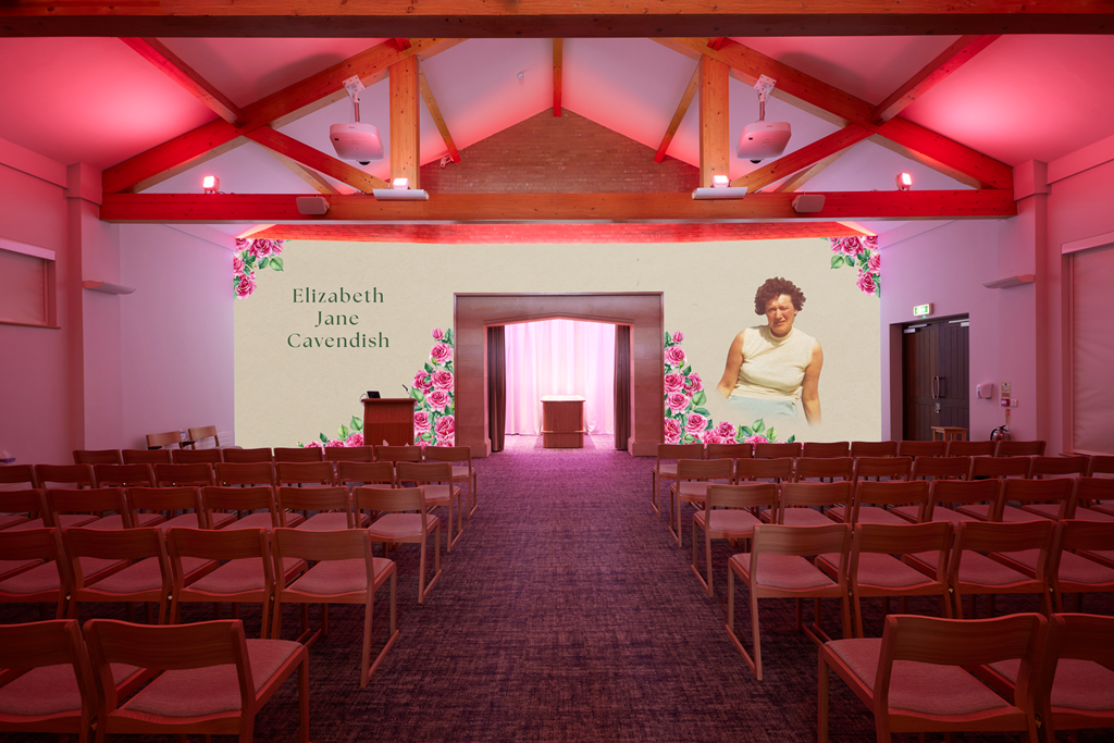 An auditorium with wooden chairs facing a stage and a large screen displaying the text 'Elizabeth Jane Cavendish' along with floral decorations and a portrait of a woman.