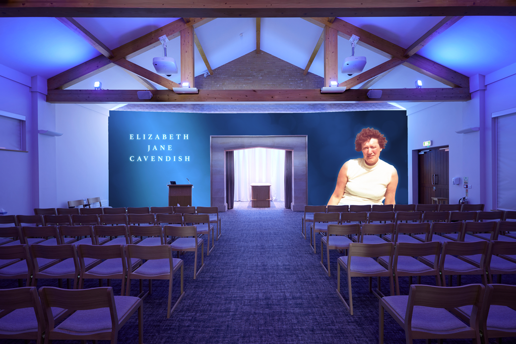 An auditorium set up for a presentation with a blue wall displaying the name Elizabeth Jane Cavendish, rows of chairs facing the stage, and a large projected image of a woman on the right side.