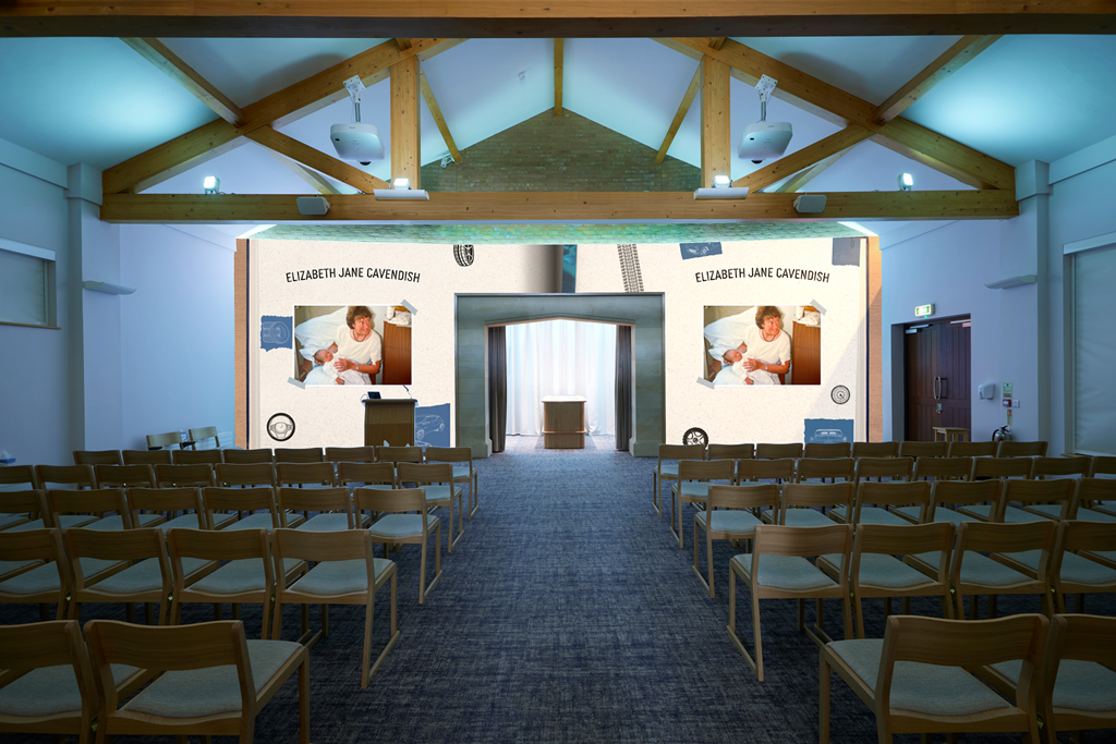A conference hall with multiple rows of wooden chairs facing a large screen displaying images and text about Elizabeth Jane Cavendish with pictures of her holding a baby, and a small stage with a podium in front of the screen.