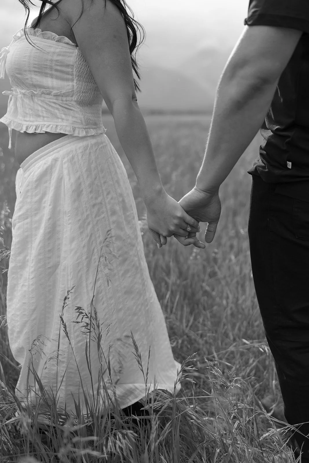 A couple holding hands in a field of tall grass.