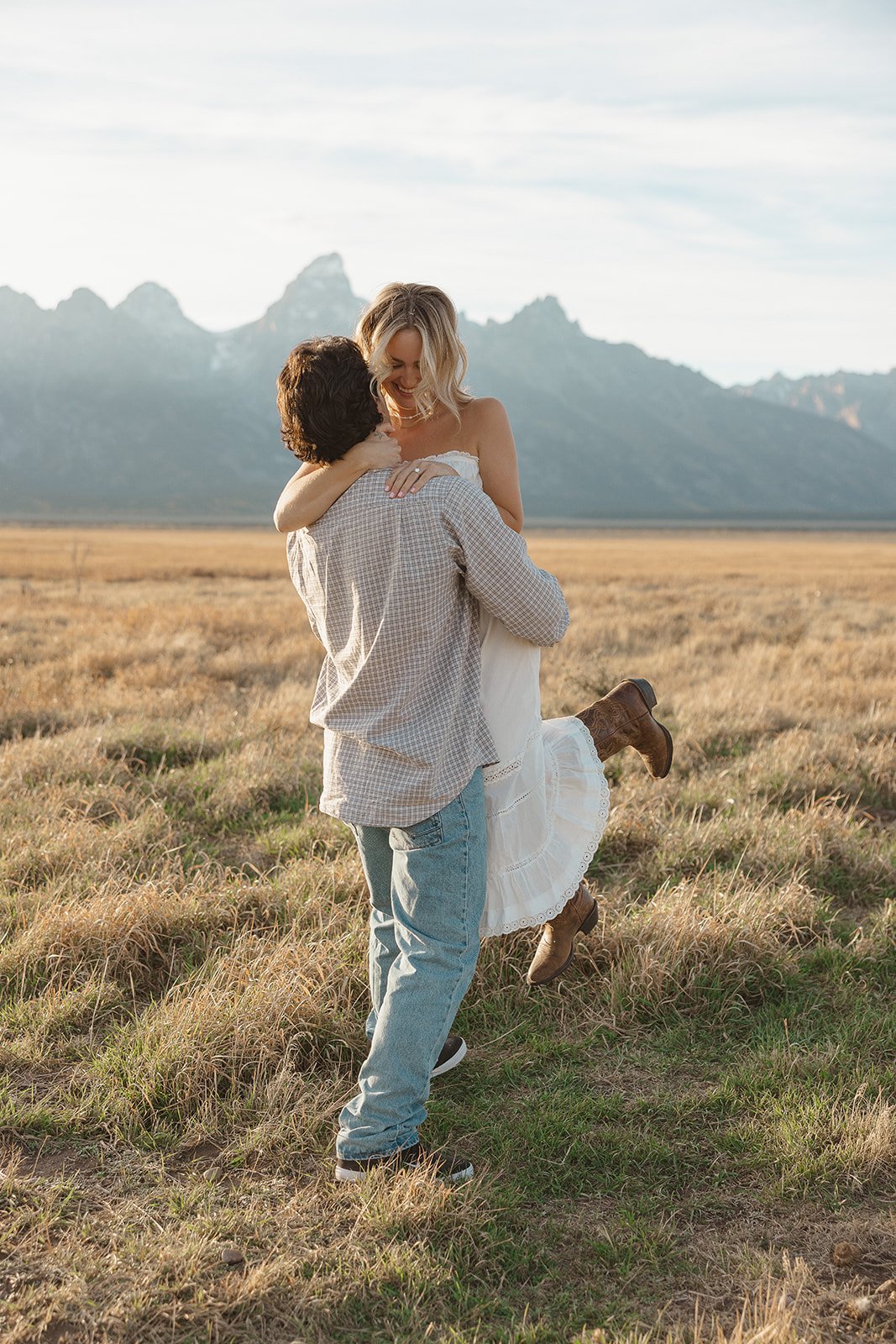 A couple in a field embracing, with mountains in the background, during daytime.