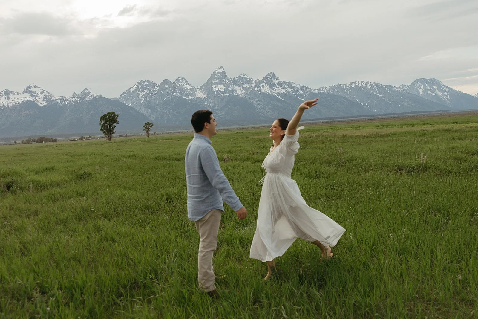 A couple dancing in a green field with snow-capped mountains in the background.