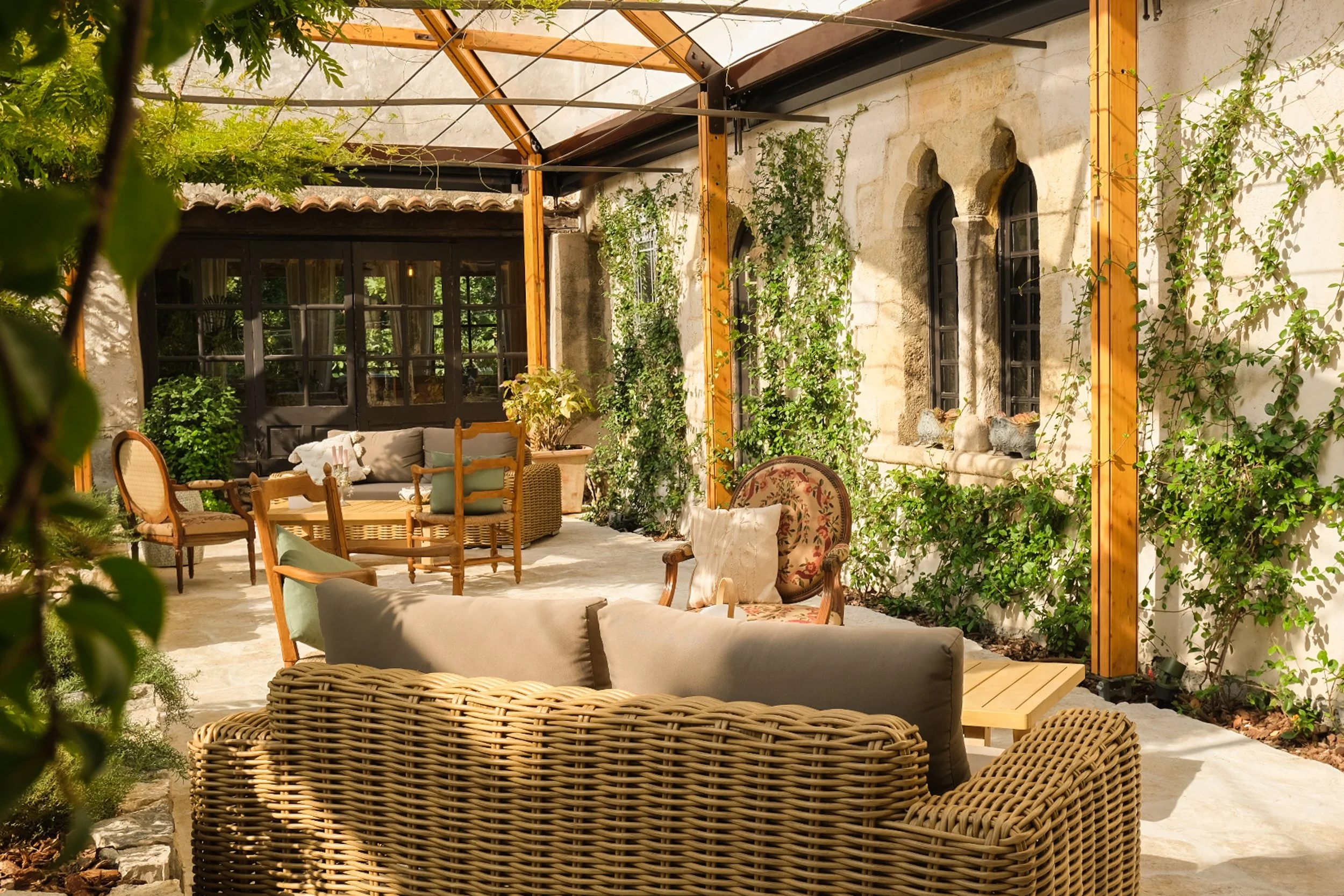 Un patio extérieur avec des meubles en rotin et en bois, décoré de plantes grimpantes, dans un style champêtre et lumineux.