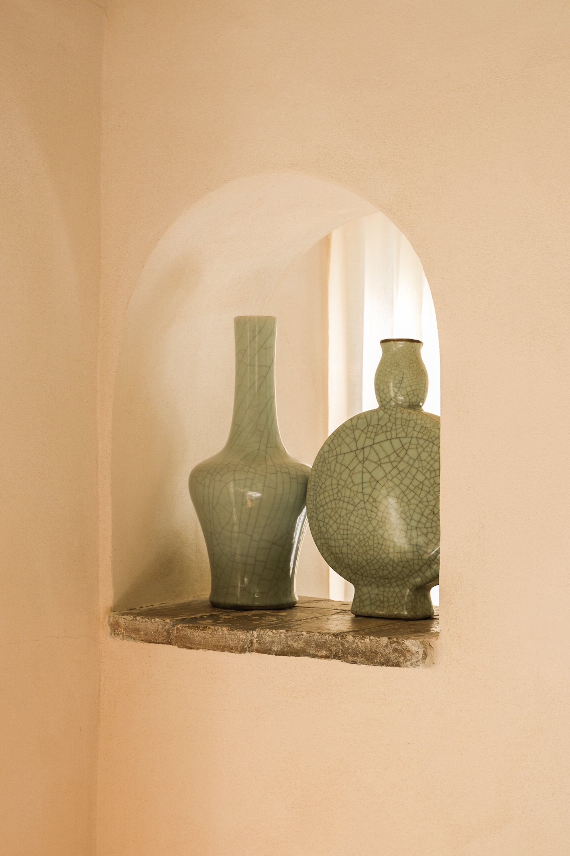 Deux vases en céramique vert craquelé placés sur une étagère en pierre dans une niche d'arc en plein intérieur.