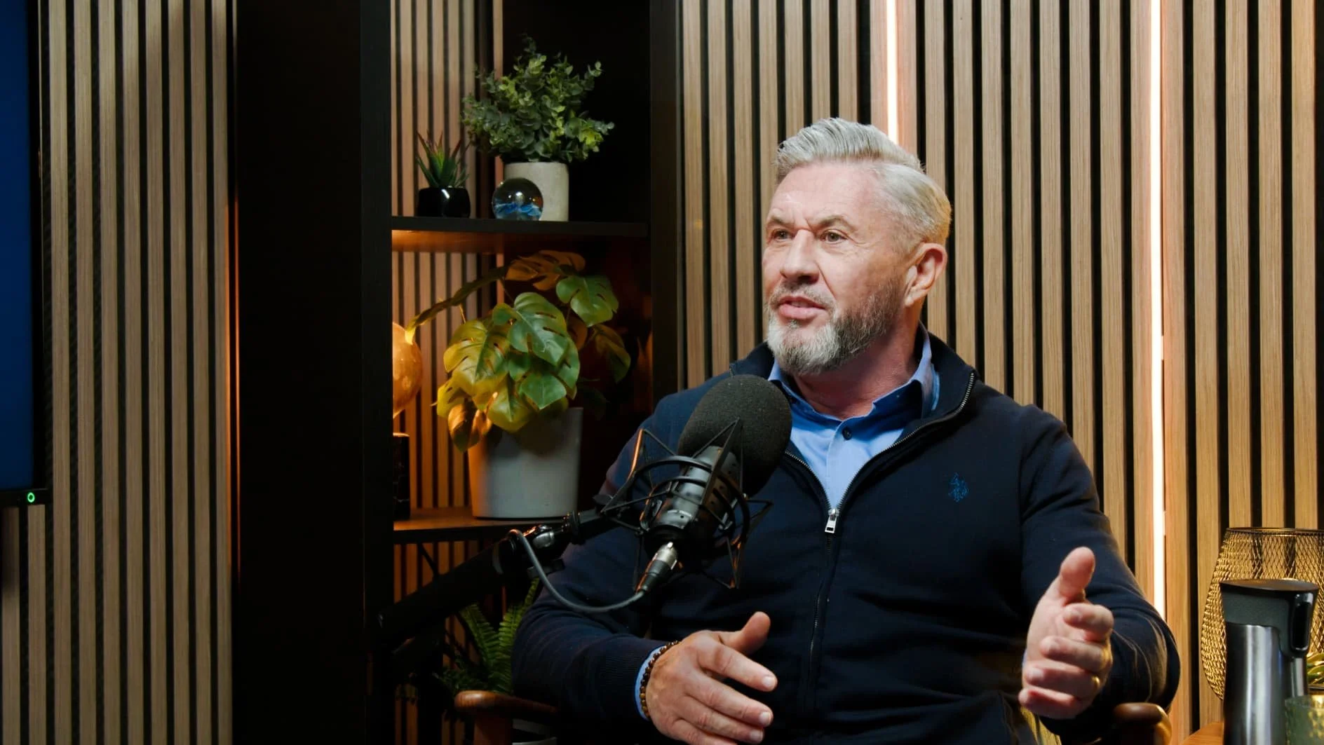 photo of a white male sitting in a podcast studio in front of a microphone recording a video podcast