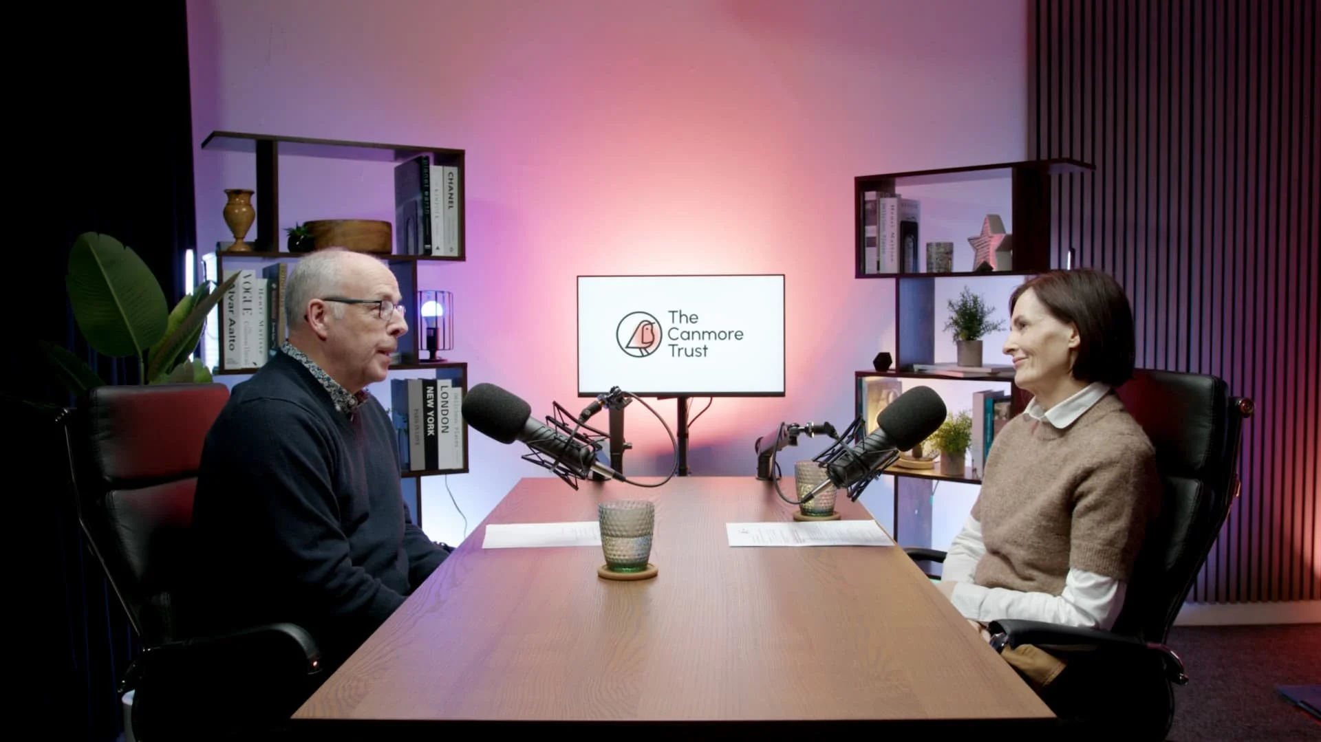 a man and a woman recording a podcast in the podcast studio glasgow, sitting at a table with microphones in front of them