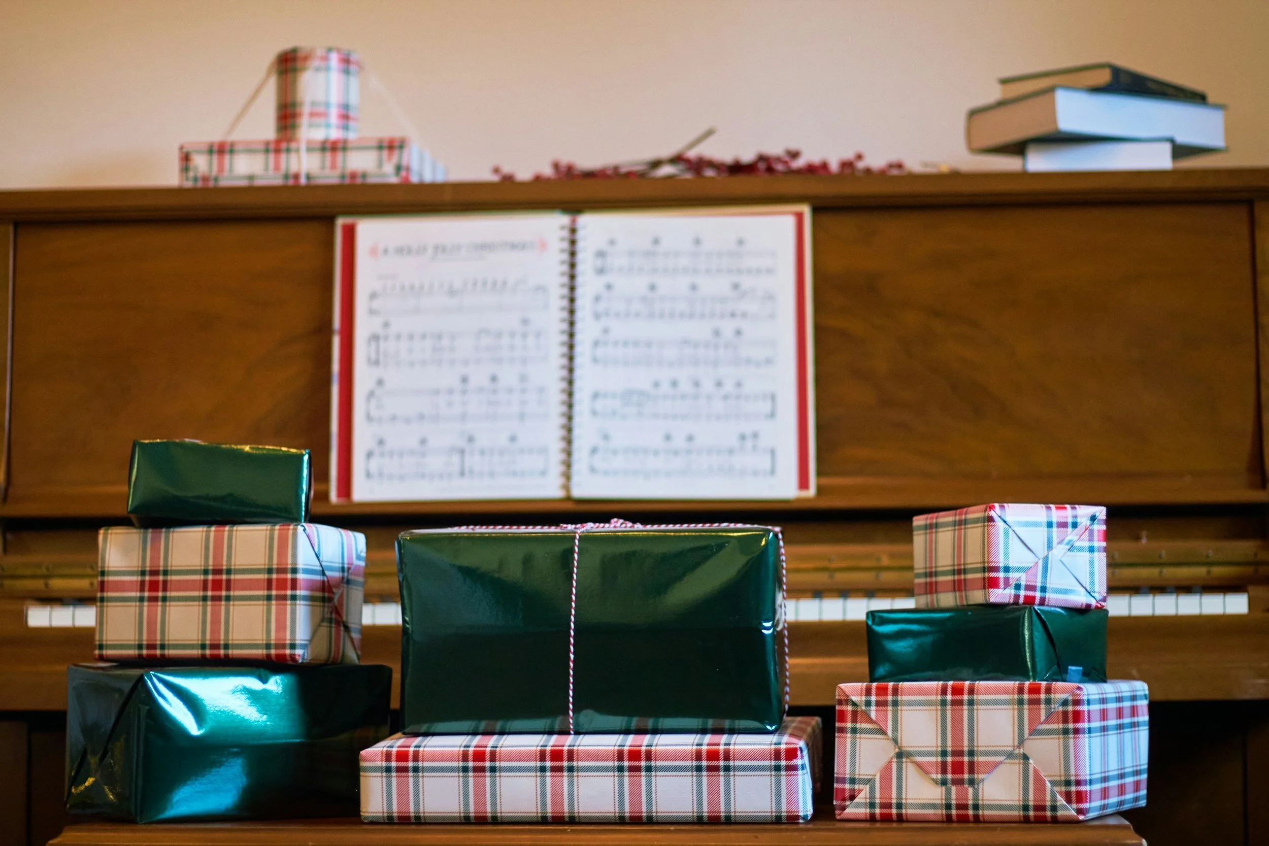 A piano with sheet music displayed, surrounded by wrapped gifts in plaid and green paper.