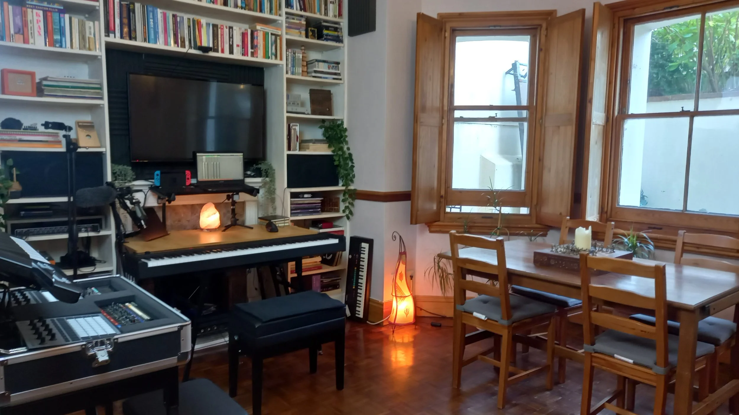 Music and dining room with piano, computer setup, bookshelves, wooden table, and chairs.