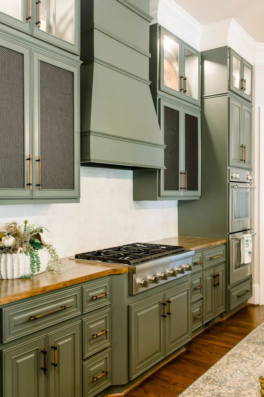 Green kitchen cabinets with gold handles, a wooden countertop, a gas stove, and built-in ovens.