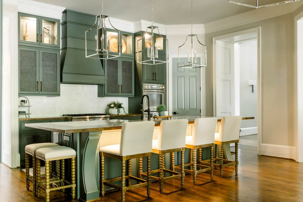Modern kitchen with green cabinets, white island with beige chairs, and pendant lighting.