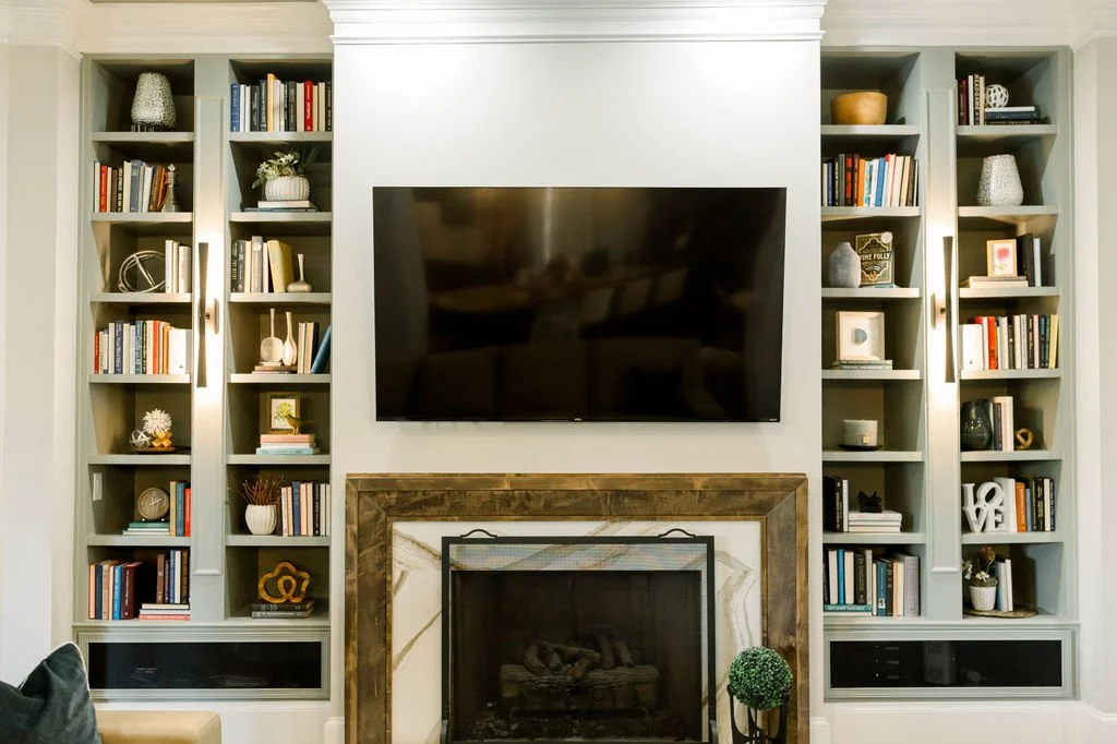 Living room with built-in bookshelves, a wall-mounted TV above a fireplace with a wood mantel, and decorative items on the shelves.