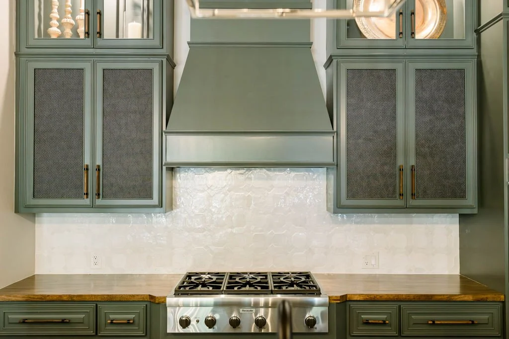 Kitchen with green cabinets, wooden countertops, a stove, a white tiled backsplash, and a stainless steel range hood.