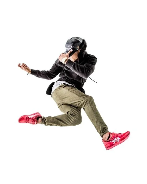 Person wearing a black hat, black hoodie, and olive green pants, jumping mid-air with red sneakers against a white background.