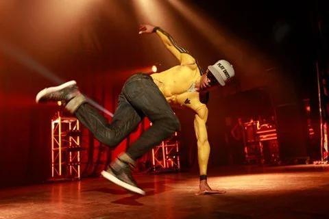 Breakdancer performing on stage with red lighting and stage equipment in the background.