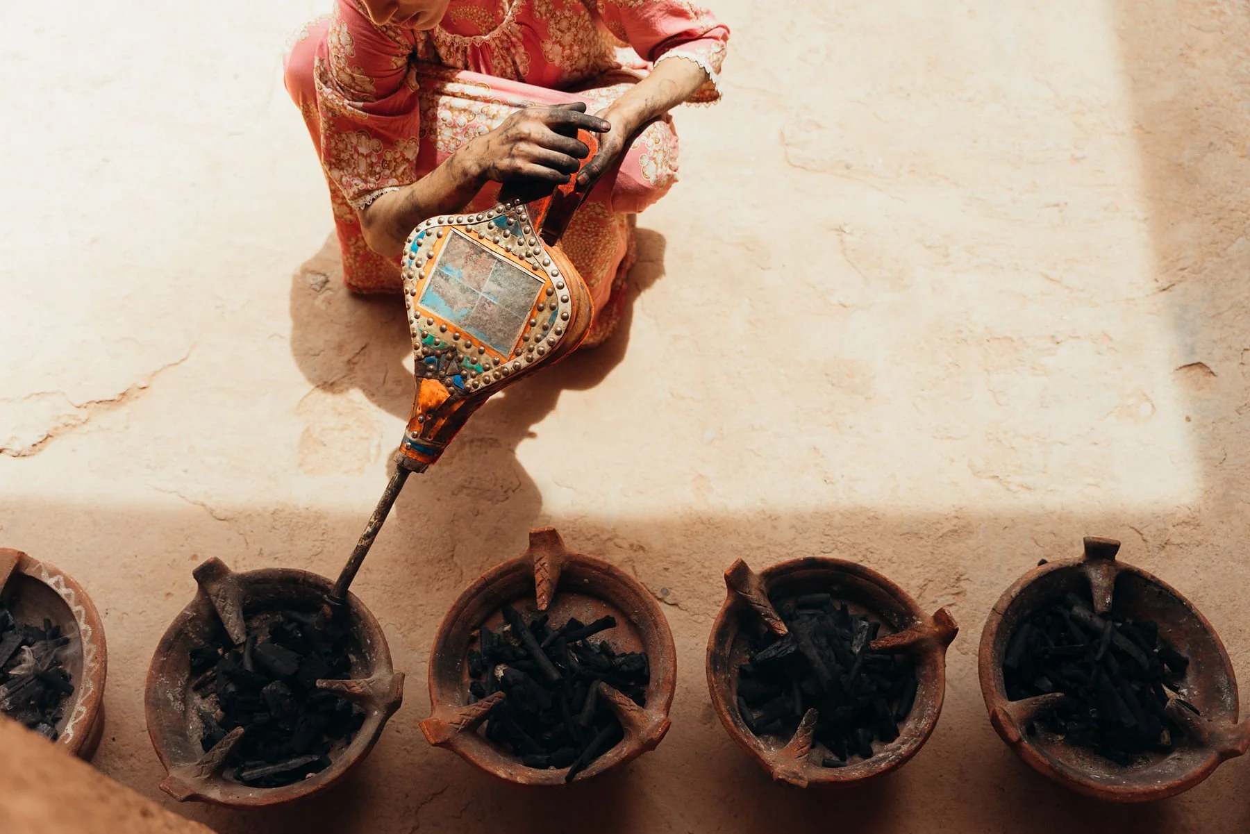 Moroccan person uses ornately decorated bellows to start fire in tagine.