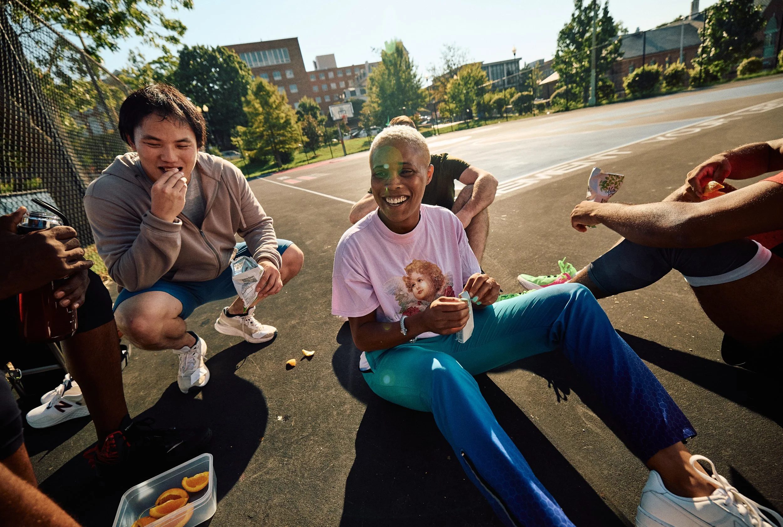 Group of friends laughing and eating snacks on outdoor basketball court during sunny day in Washington DC lifestyle photography