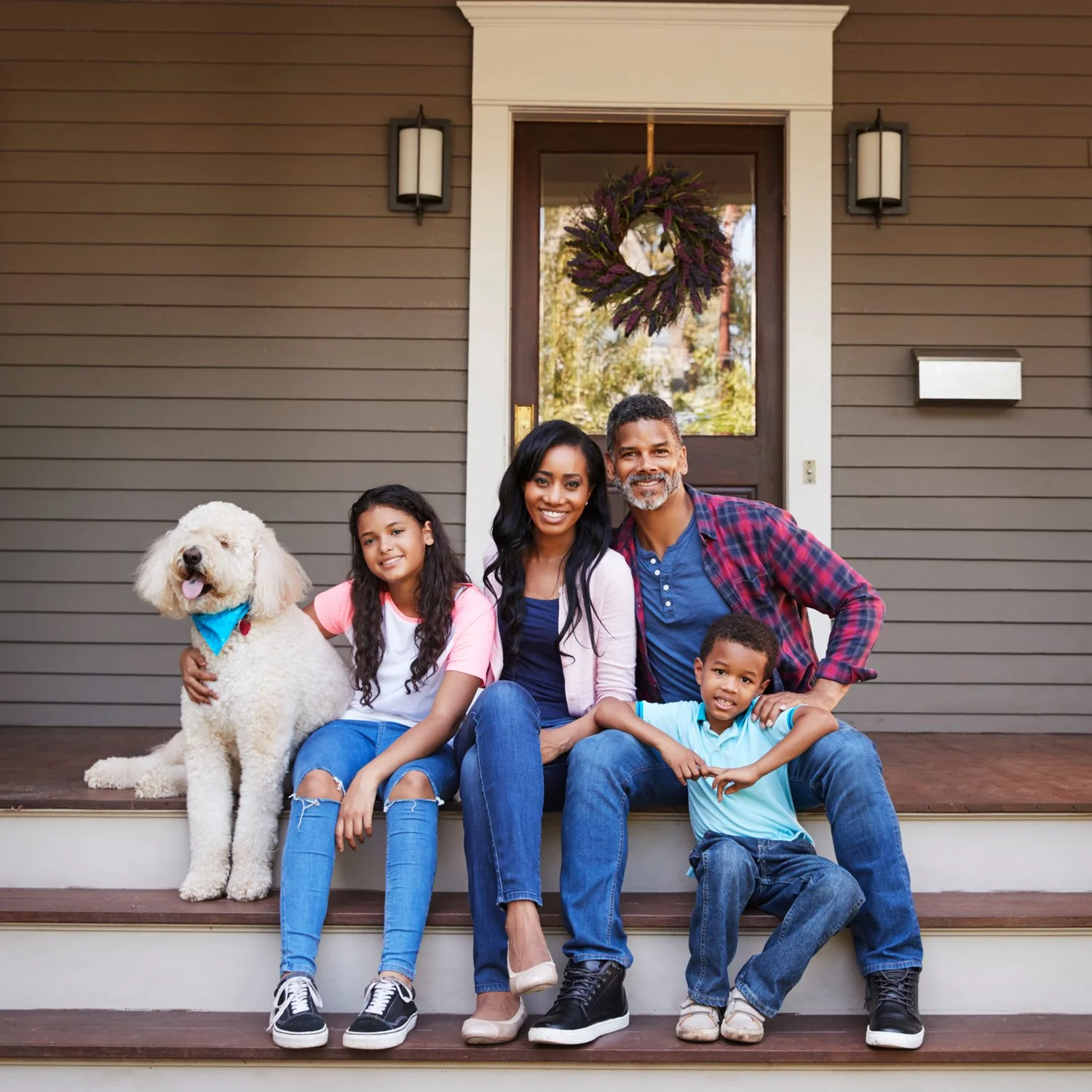 African-American family with dog sitting on steps of a brown house.