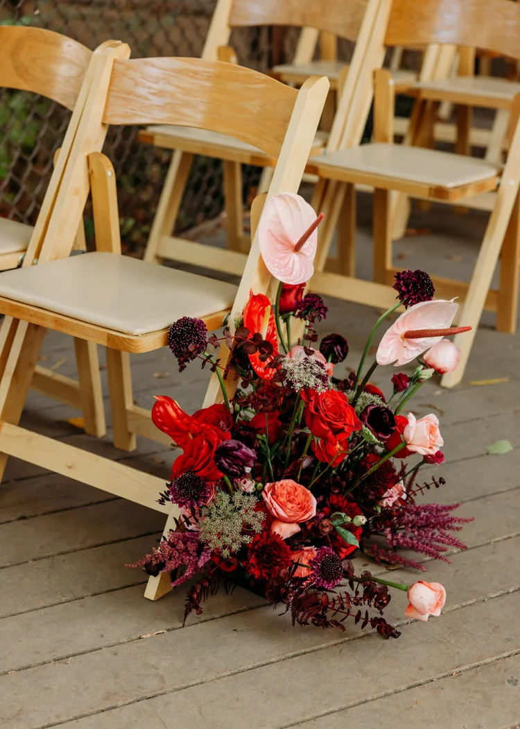 Red and burgundy aisle arrangement beside wooden ceremony chairs