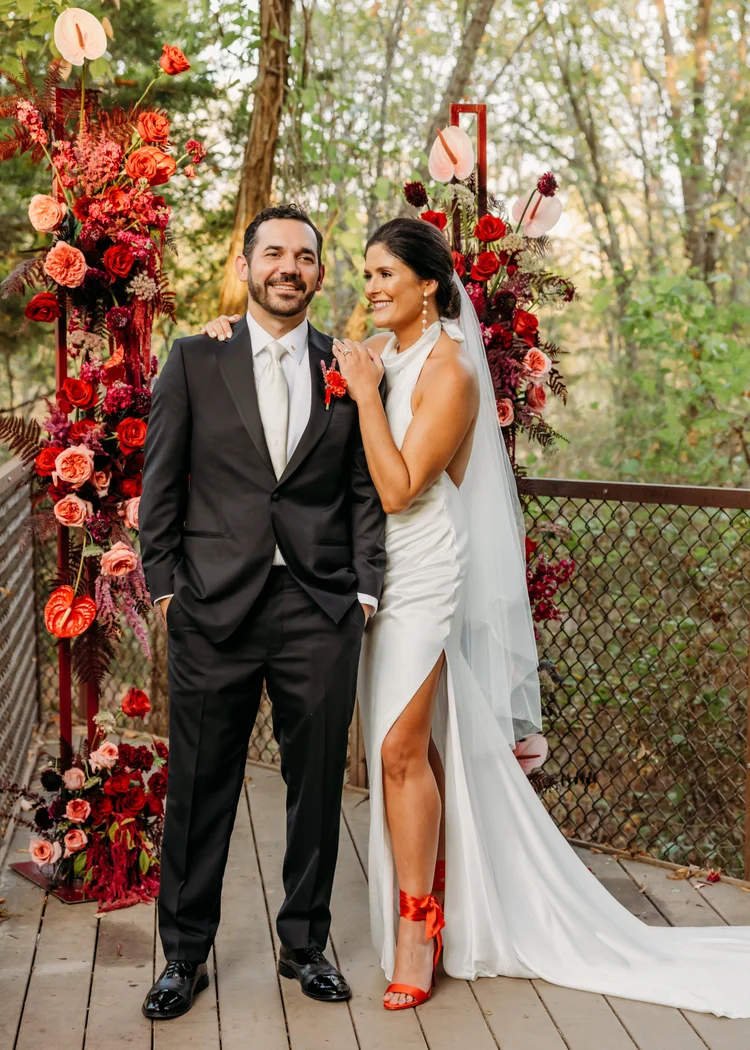 Bride and groom in front of a red and pink floral ceremony arch