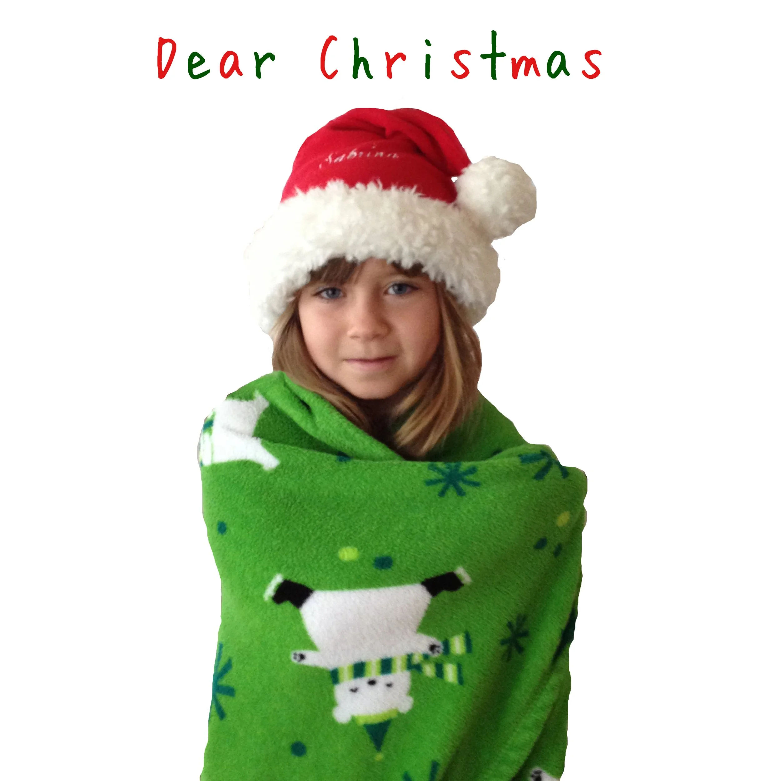 A young girl wearing a Santa hat and a green Christmas blanket with snowmen and snowflakes, standing against a white background with a greeting that says 'Dear Christmas' in colorful letters.