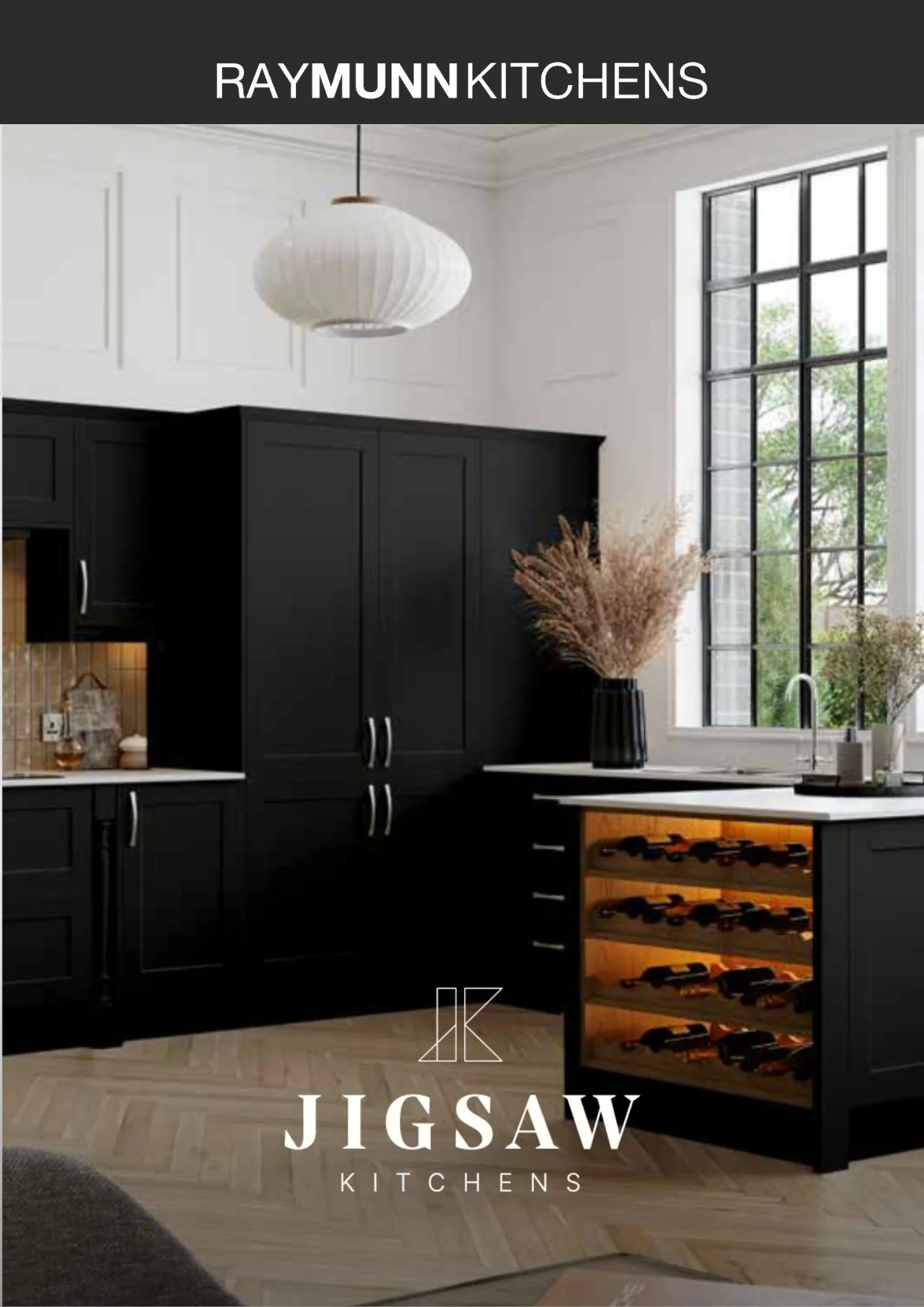 Modern kitchen interior with a black island counter dark cabinetry. Includes integrated oven and microwave, a sink with chrome faucet, and small plant decor. RayMunn Kitchens branding at the top and Jigsaw logo at the bottom.
