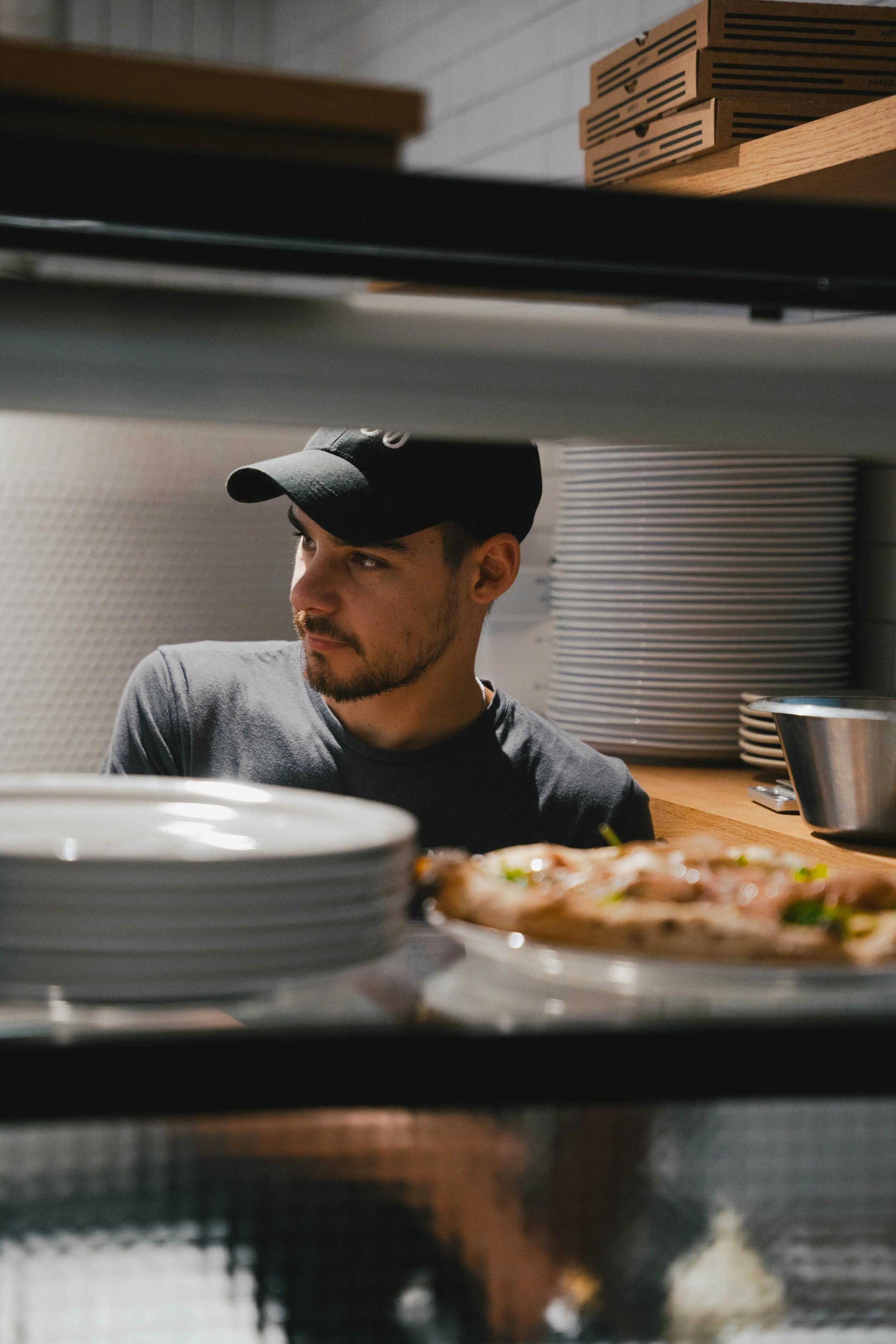 Jeune homme regardant à travers une ouverture dans une cuisine, avec des assiettes et une pizza en avant.