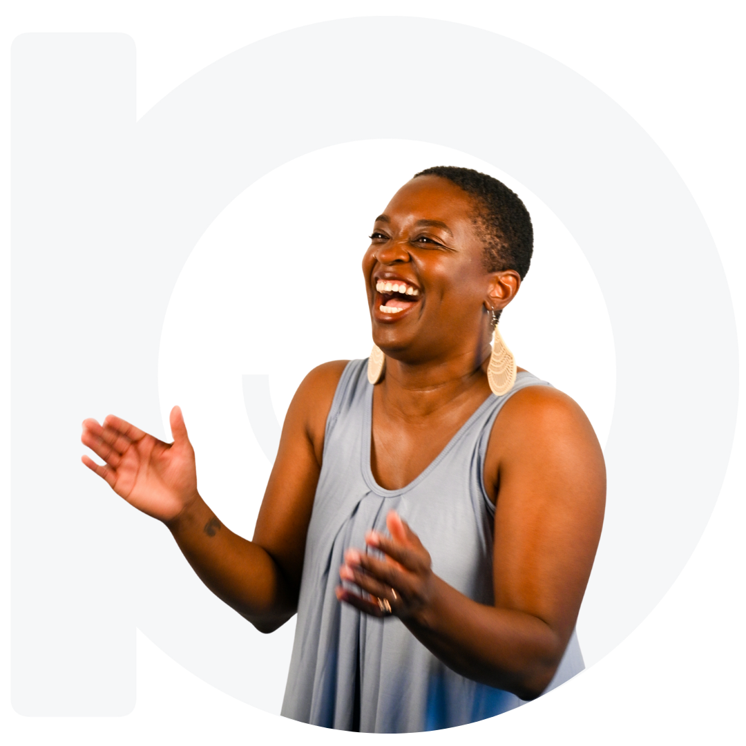 Tamisiha is in loose fitting light blue dress. She's laughing and clapping. The company logo is behind her in white.