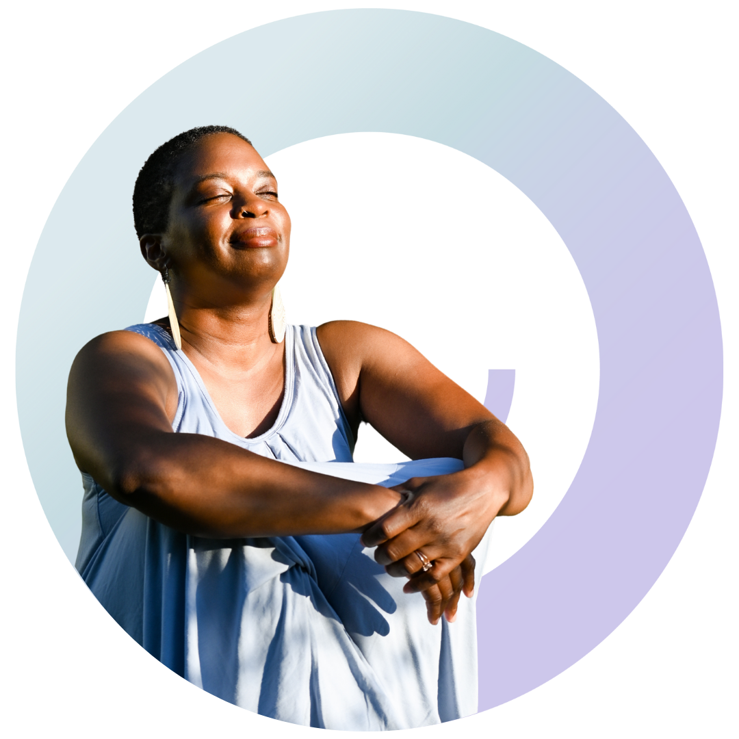 Tamisha is wearing a loose fitting light blue dress. She's smiling towards the sky and her eyes are closed. The company logo is behind her.