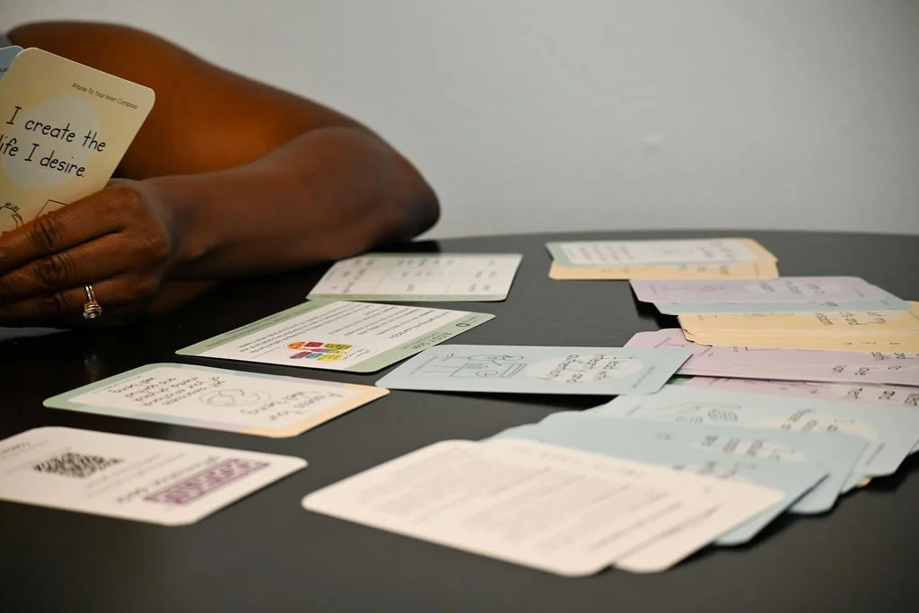 Tamisha is holding affirmation cards in her hands and several affirmation cards are spread out on the table.