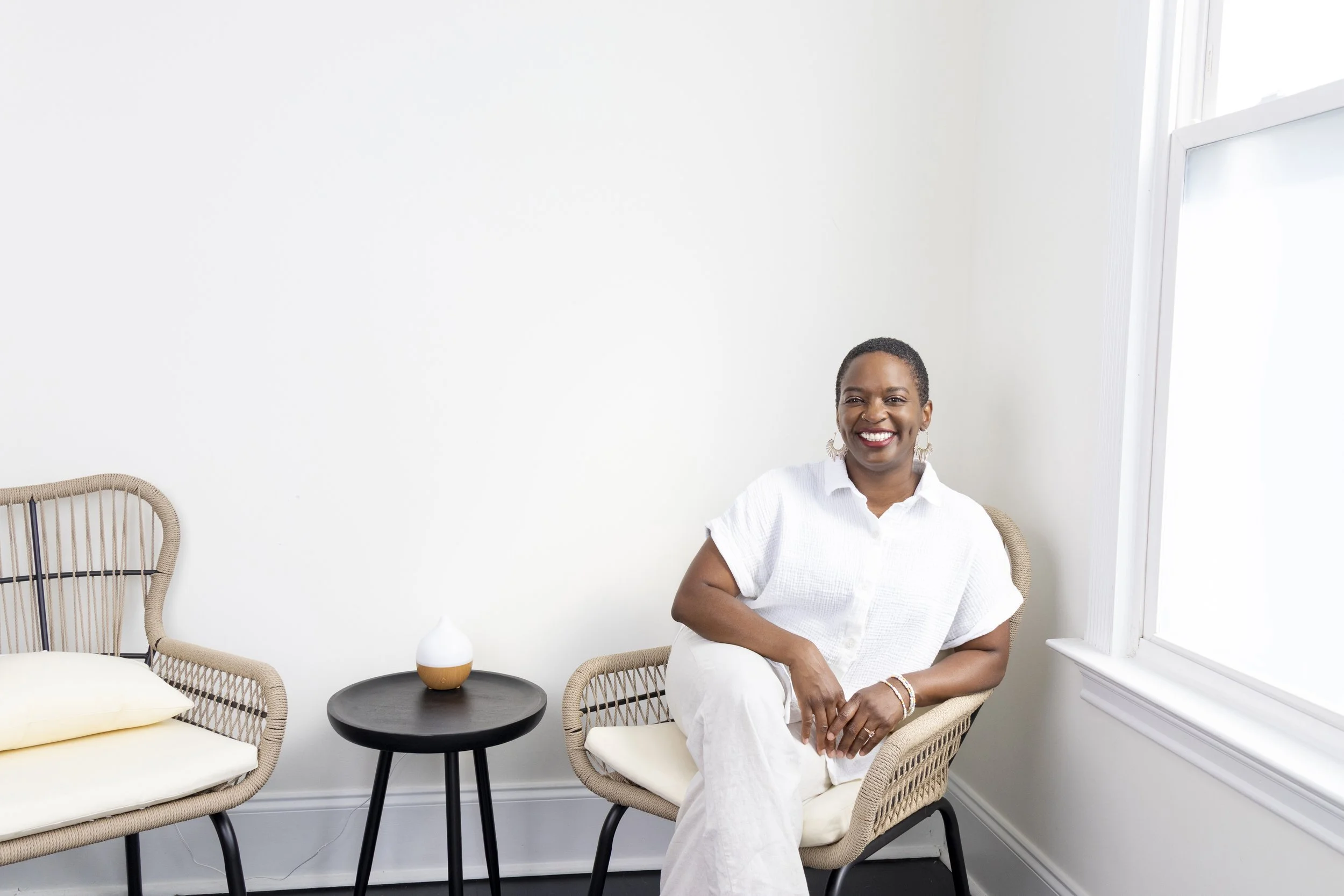 Tamisha is wearing a white top and khaki pants. She's sitting in a wicker chair