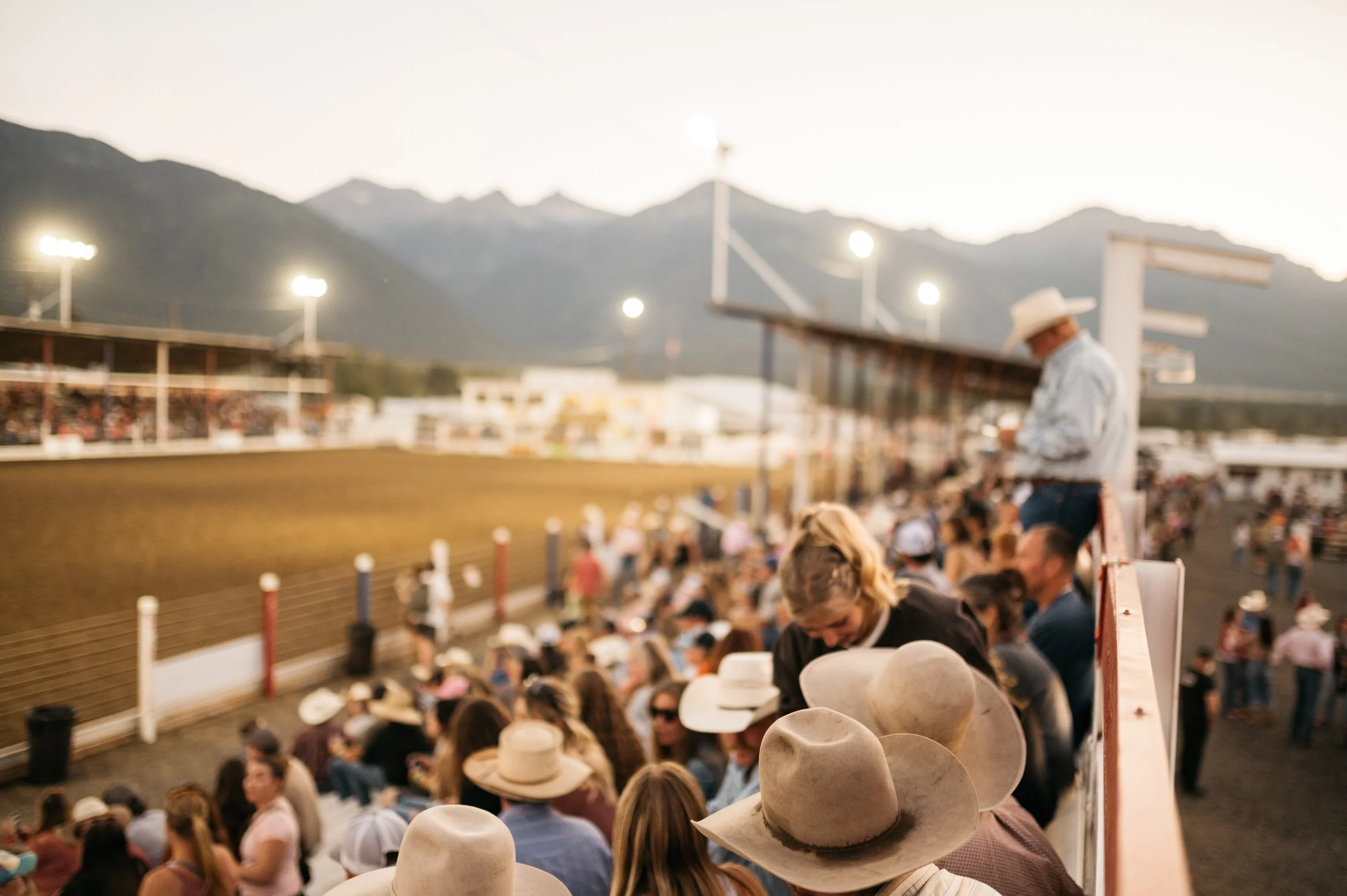Crowd watching a dirt race track at sunset with mountains in the background.