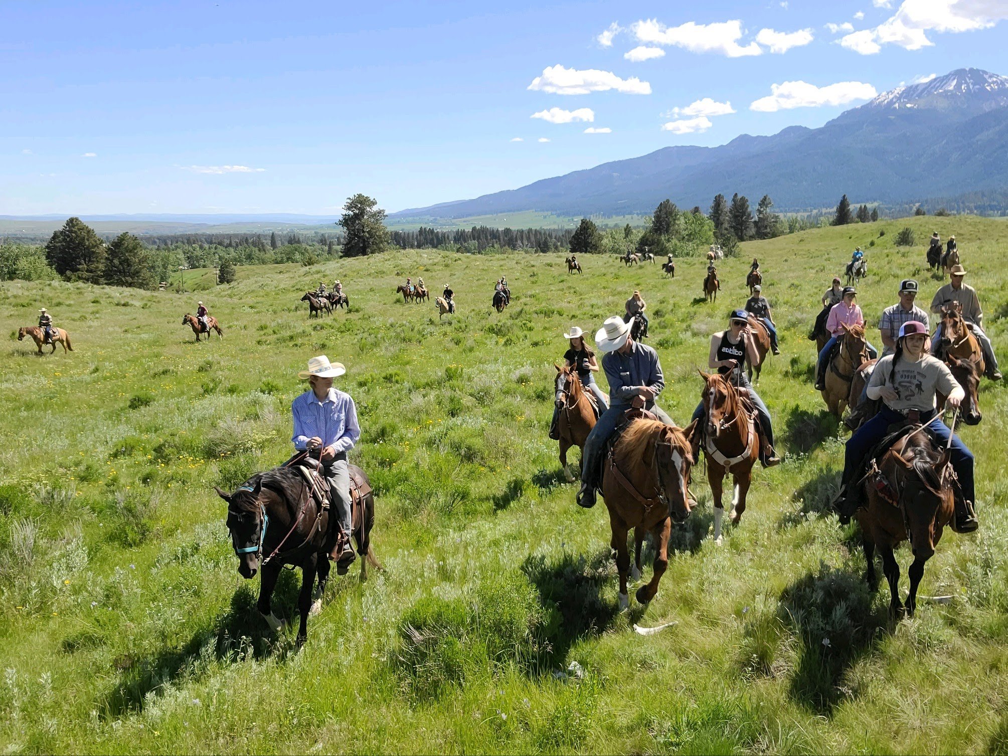 Group of people horseback riding in a green field with mountains in the background.