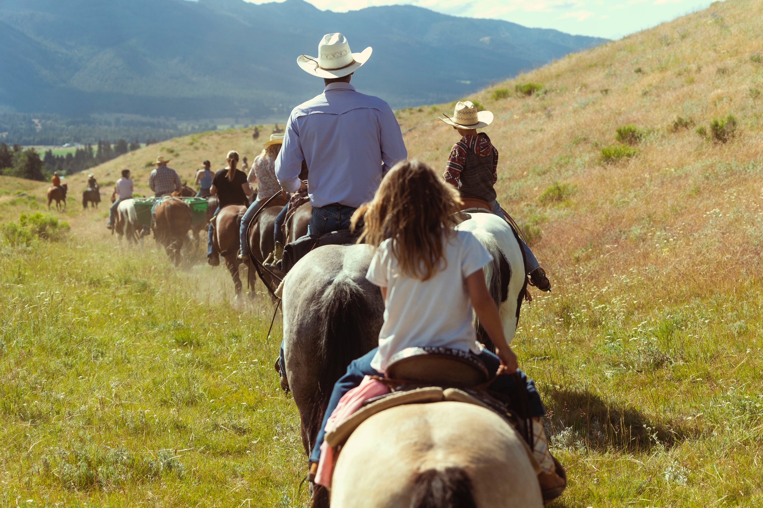 Group of people horseback riding on a grassy trail in a hilly landscape.