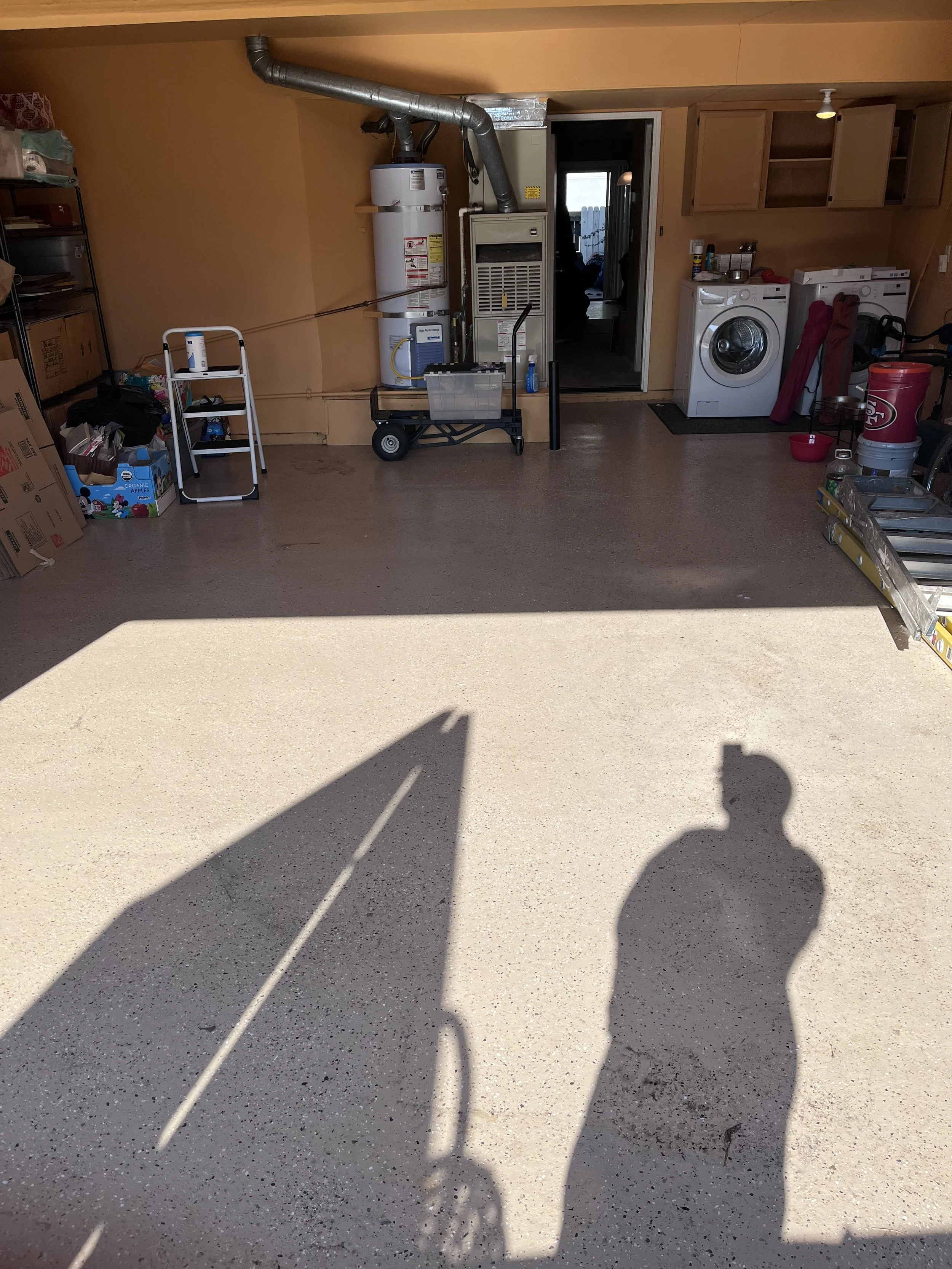 Garage interior with washer and dryer, shelves, storage boxes, and sunlight casting shadows on the floor.