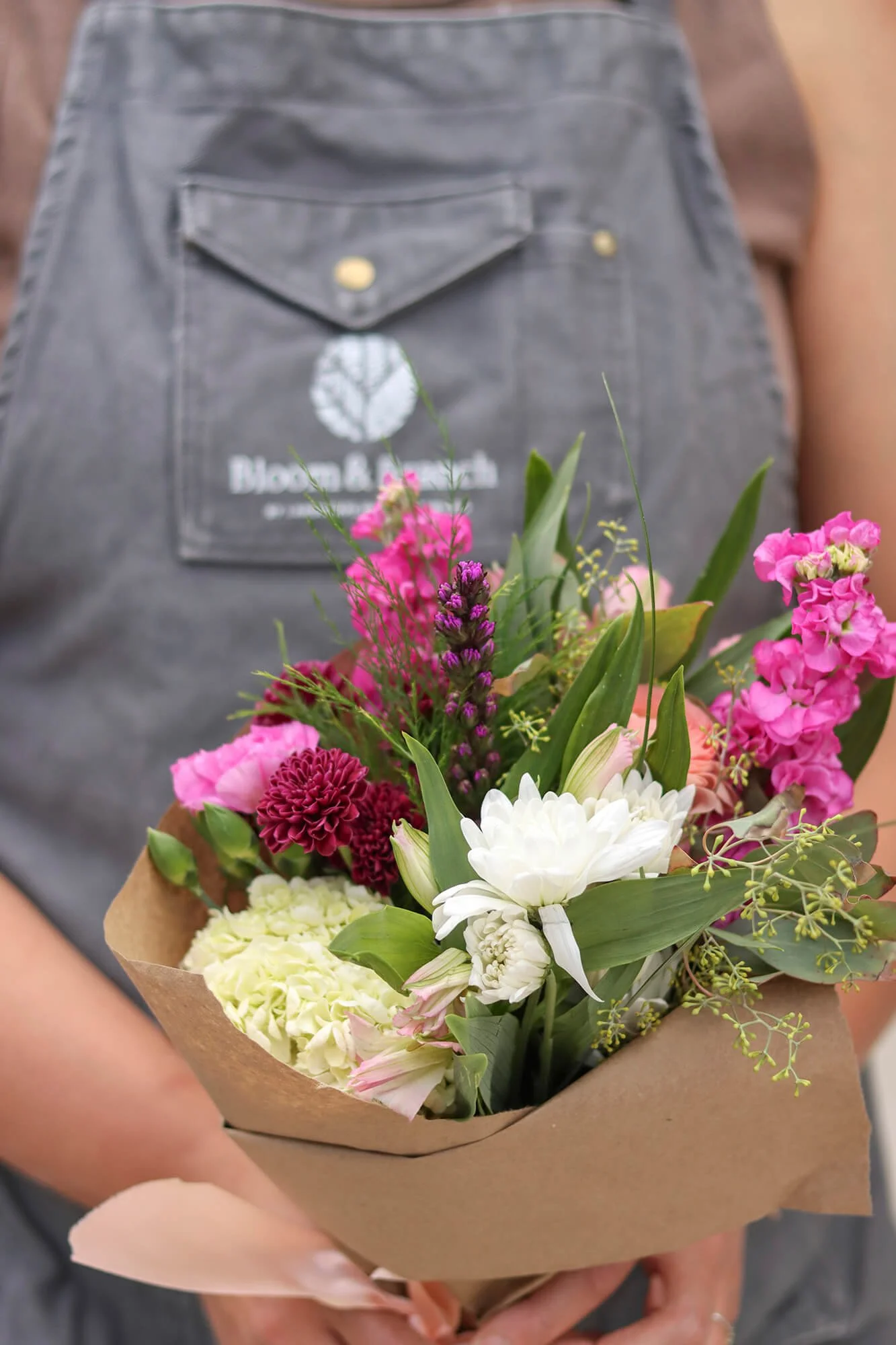 a worker in a bloom & branch apron holding a bouquet of flowers
