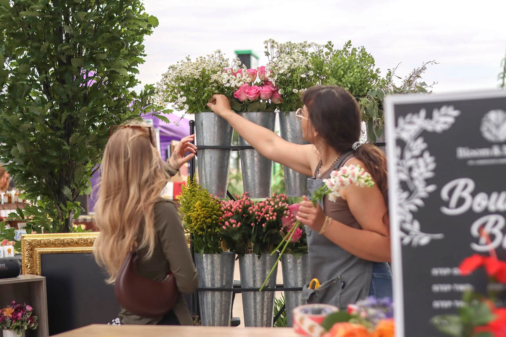 two women picking out flowers from aluminum tin holders