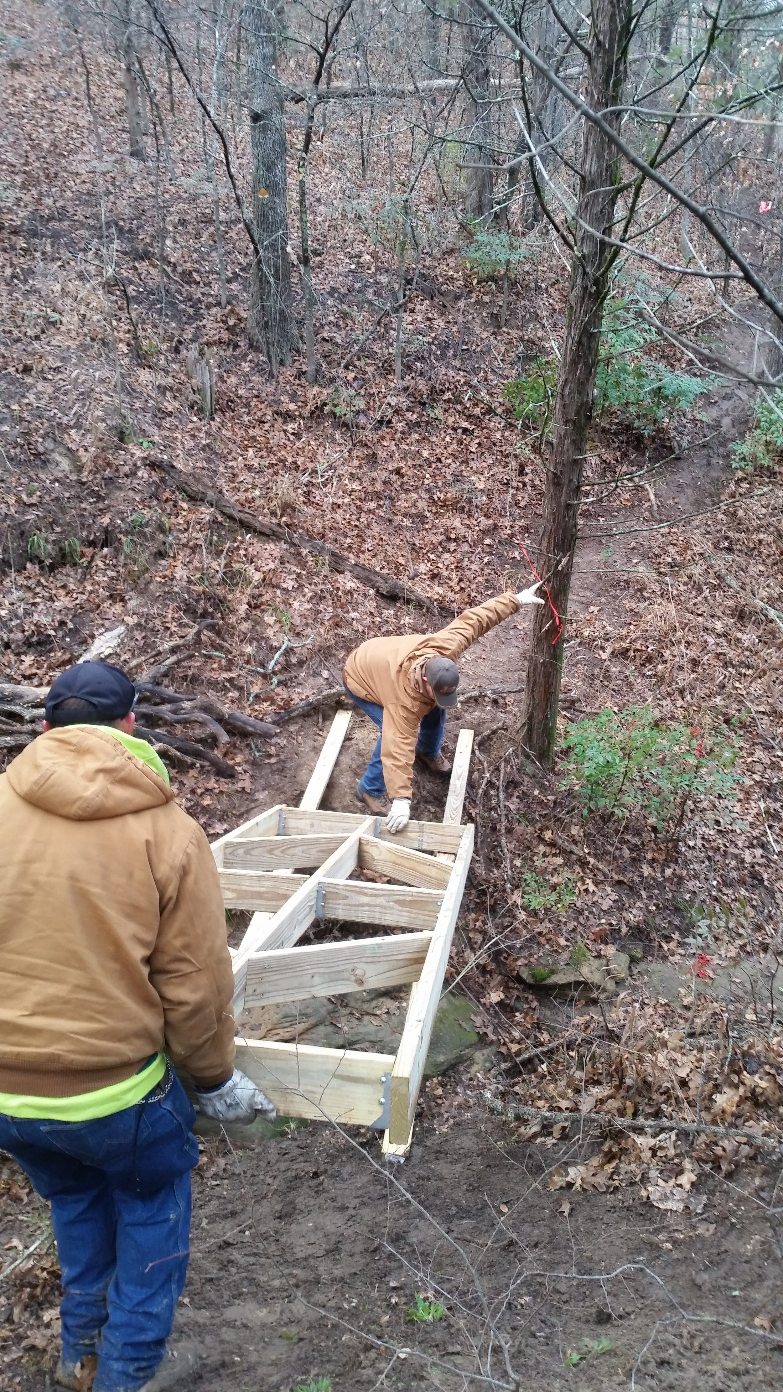 Trail bridge structure being put in place by two volunteers.