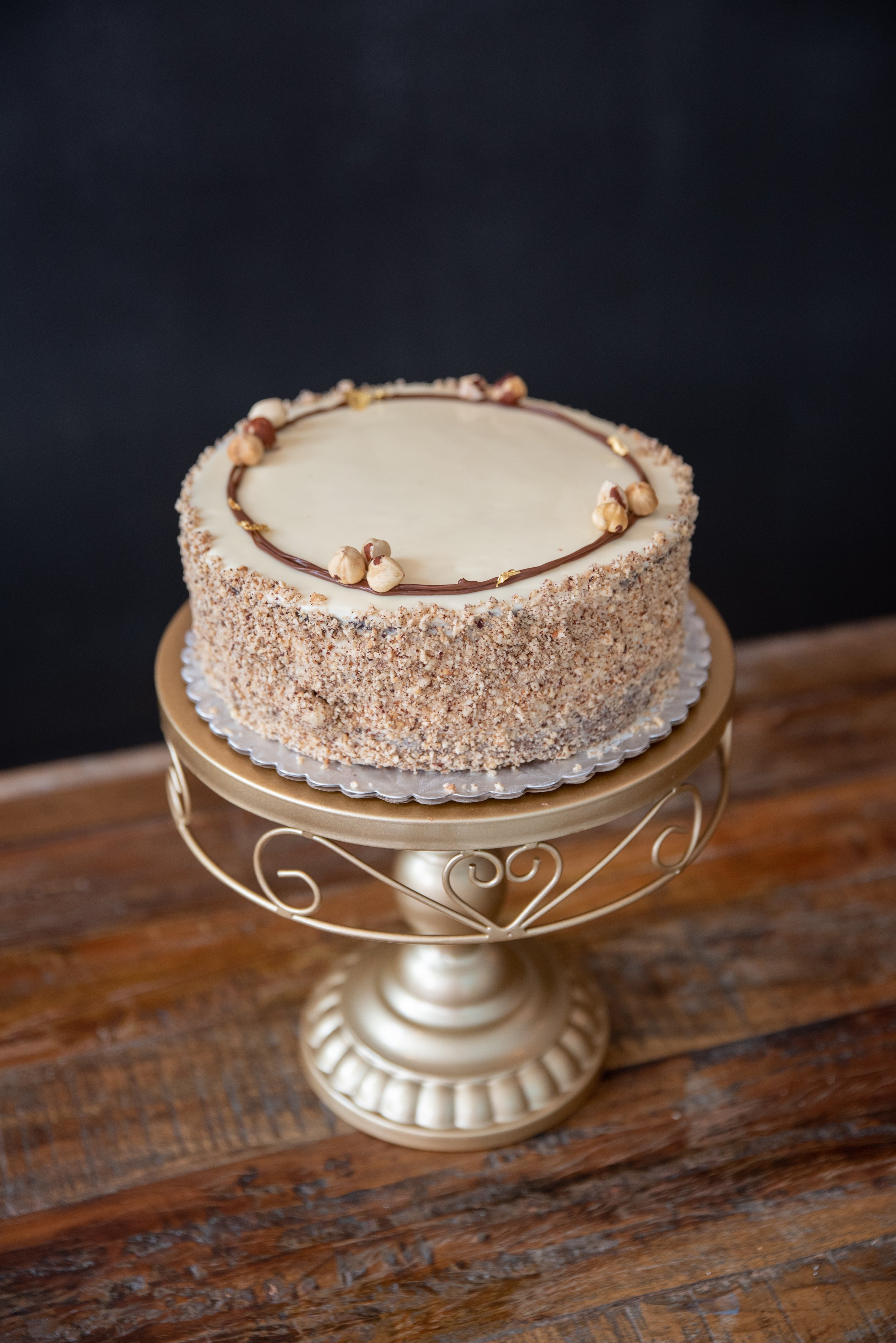 NUTELLA - Vanilla cake with Nutella cream filling. Polished with white chocolate ganache and coated with hazelnuts.