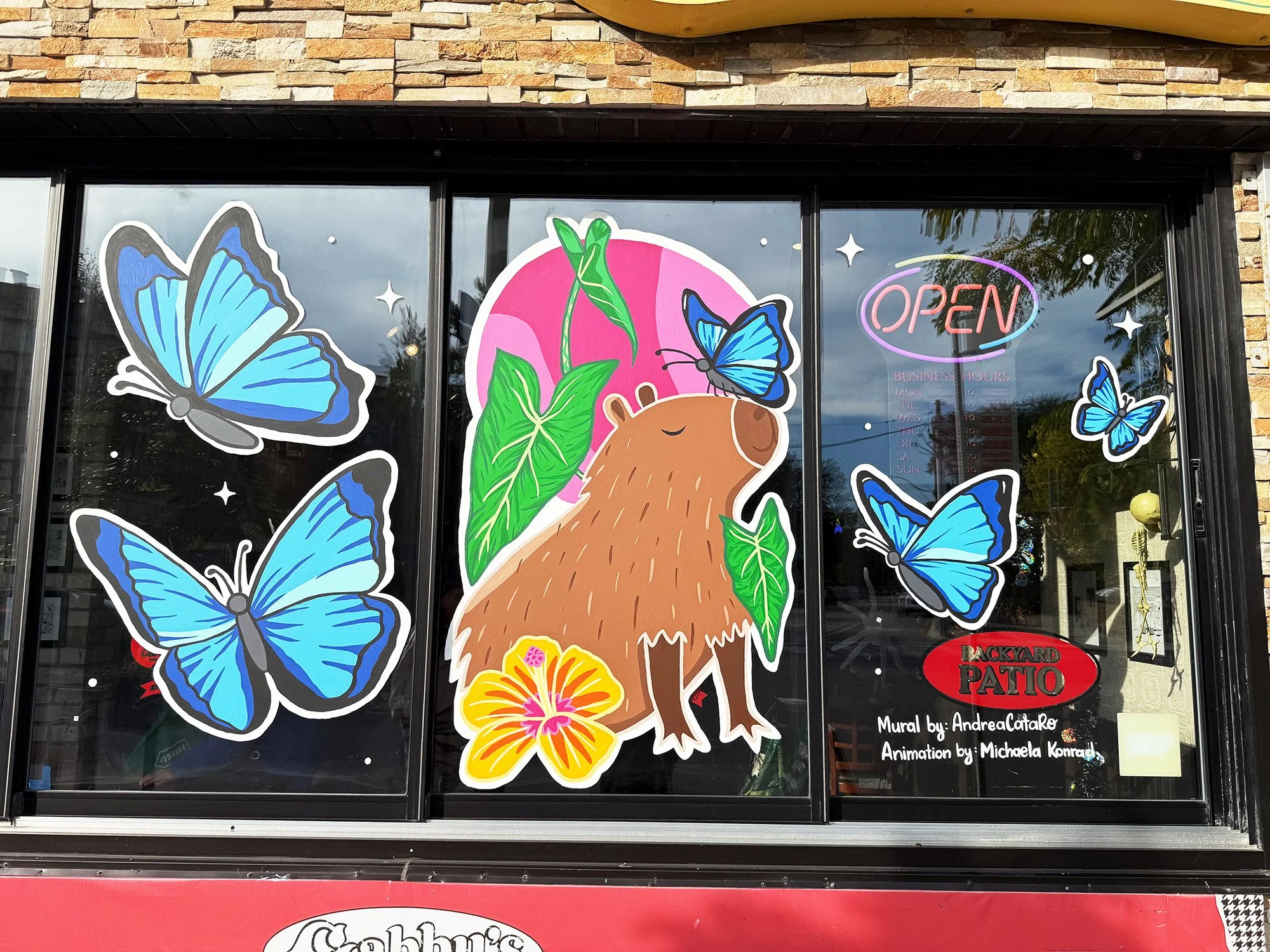 Capybara and blue morpho butterfly window mural at Gabby's for Window Wonderland