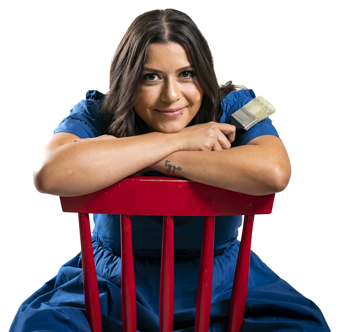 Toronto Muralist in blue dress leaning on red chair, holding a paintbrush.