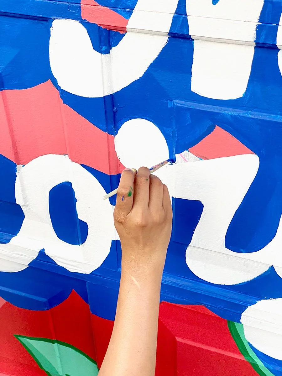 Close up of mural painting in progress showing hand painted lettering and colour blocking