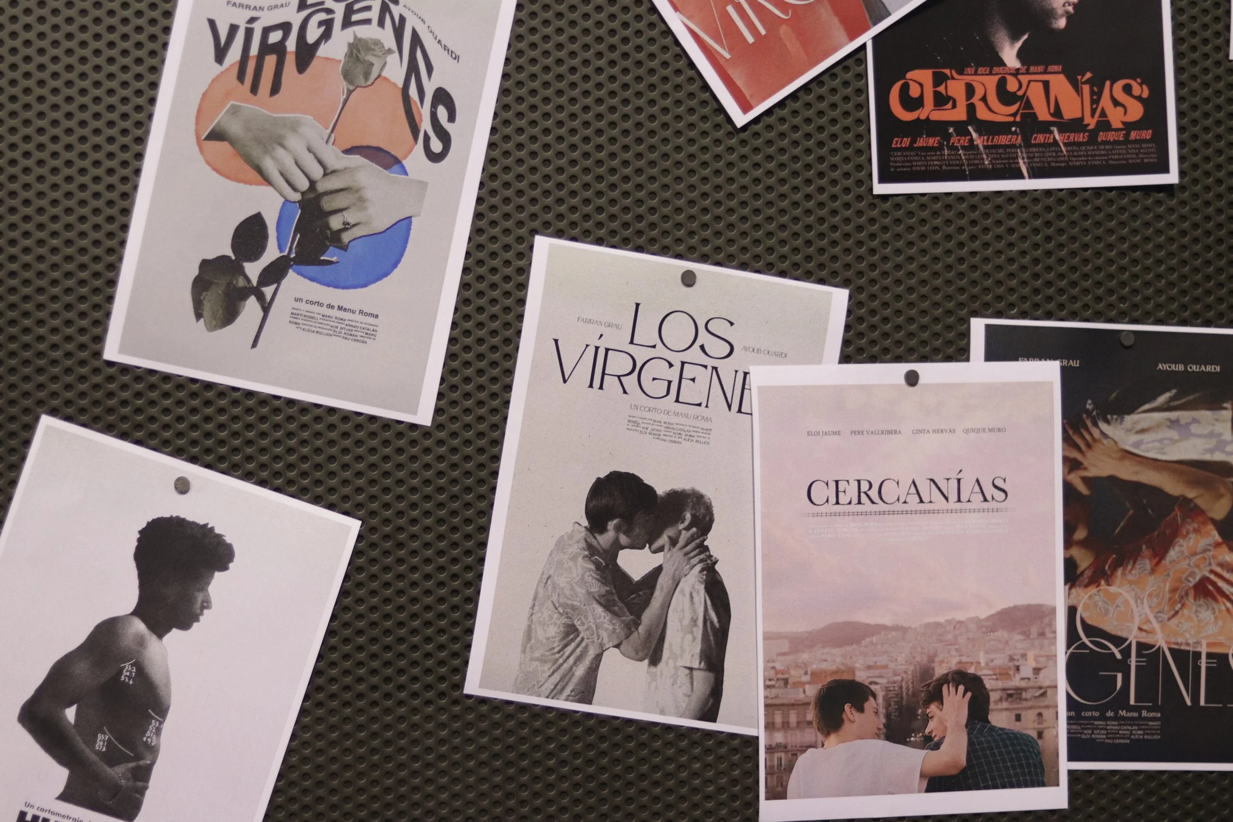 Varios carteles de películas cortas en papel sobre una superficie perforada. Incluyen imágenes artísticas y textos en español como "Los Vírgenes" y "Cercanías". Algunos muestran siluetas y escenas de personas interactuando.