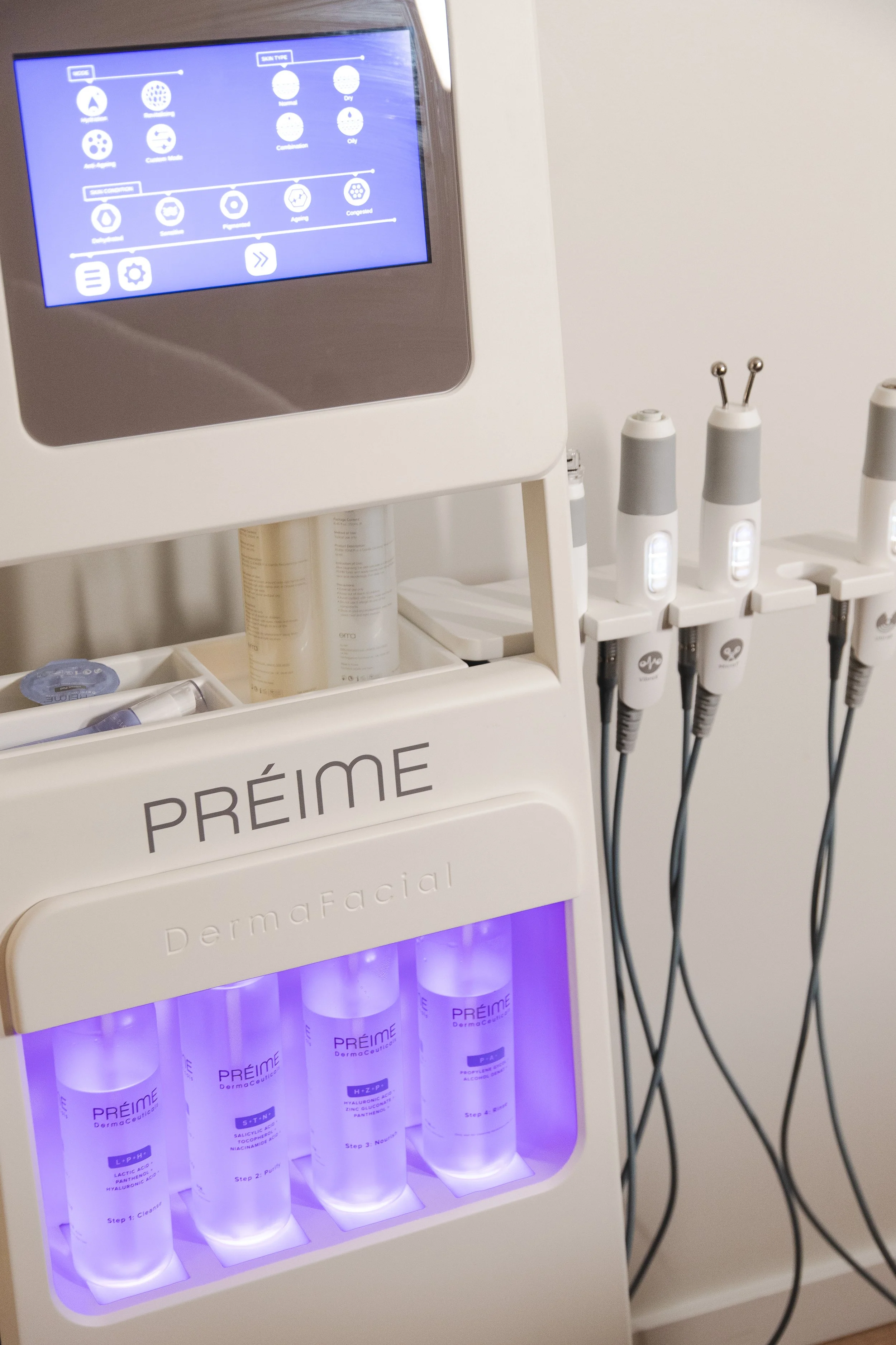 Medical aesthetic device named PRÉIME with four bottles labeled for skin care steps, connected to multiple handpieces, in a clinical setting.