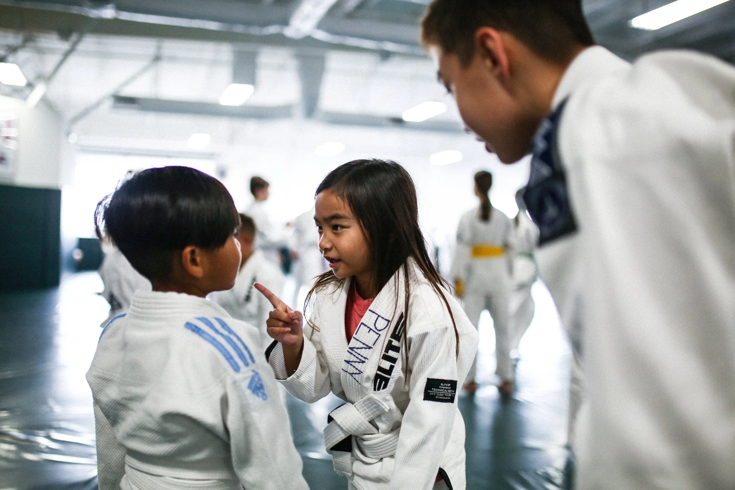 Young girl in a white martial arts gi instructs two boys in a martial arts training gym.