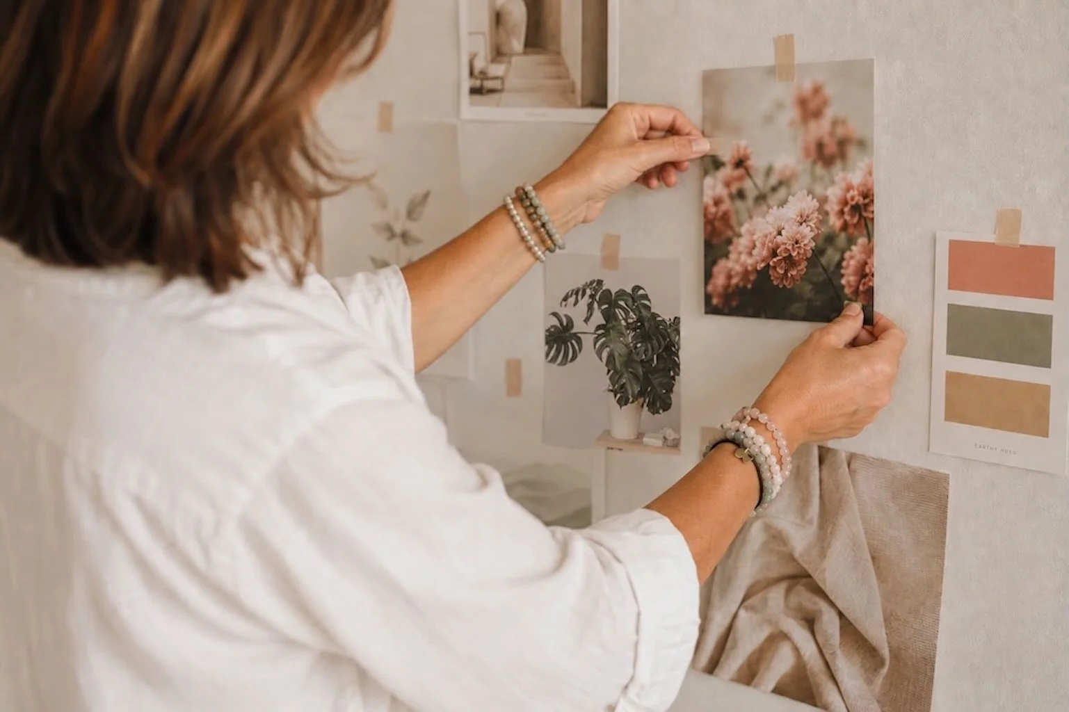Marta taping a peach-colored flower photo on a wall decorated with other photographs and color swatches.