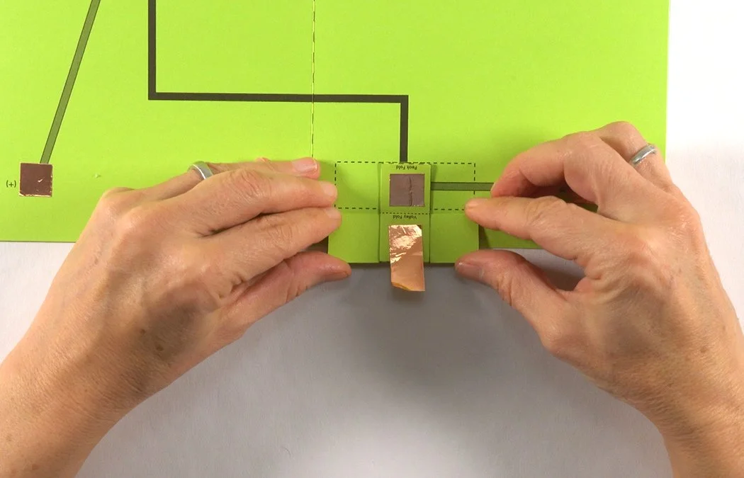 Stick the copper directly over the grey (+) rectangle inside the battery box. Do not get either copper piece close to your dashed fold line.