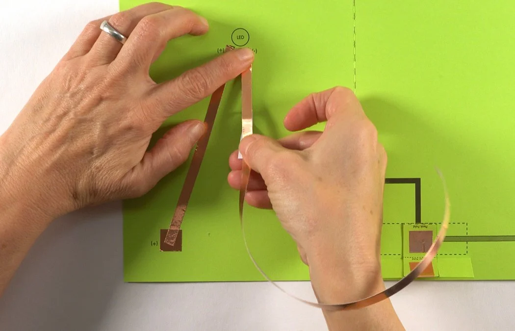 Starting under the LED circle, stick the copper to the black (-) diagram. Do not place copper inside the LED circle.